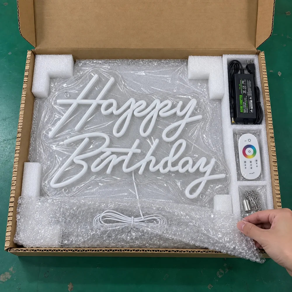 Happy Birthday neon sign wrapped in clear protective film and foam, with its power adapter and remote.