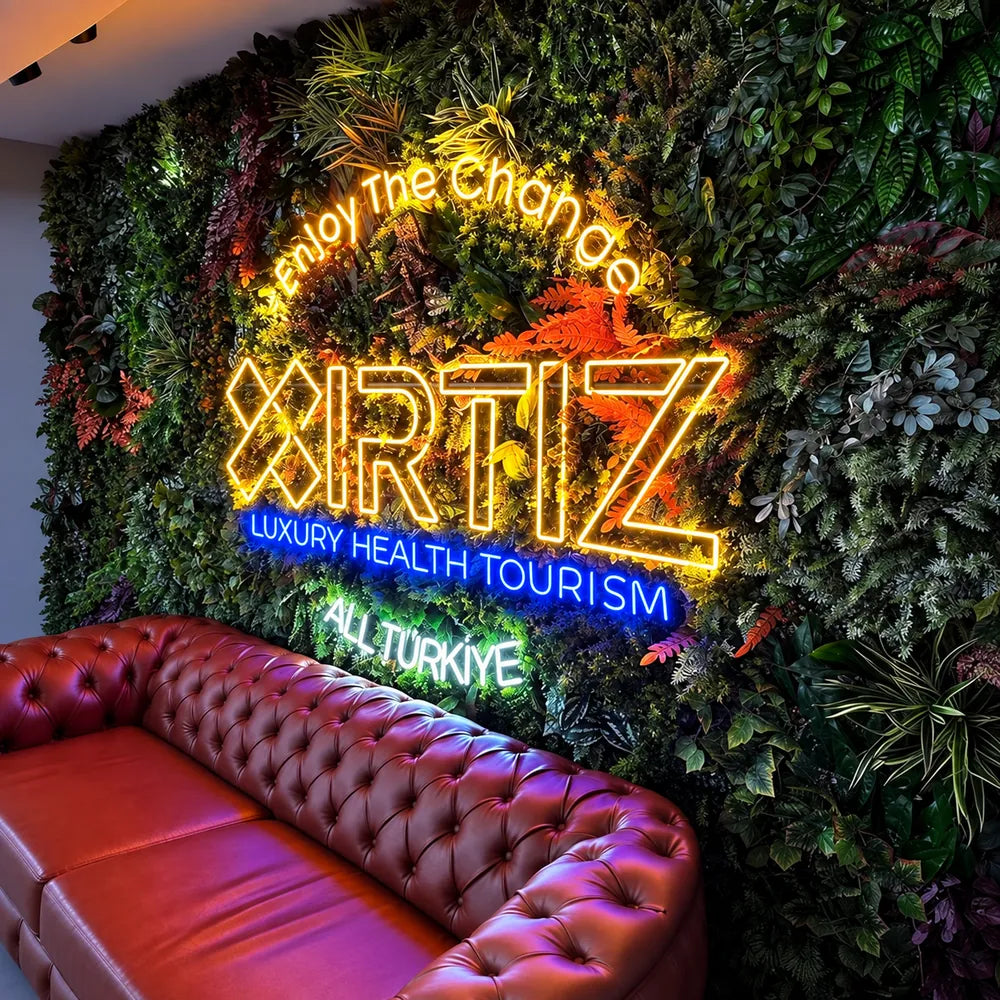 Large yellow and blue custom neon sign on a green plant wall above a red sofa.