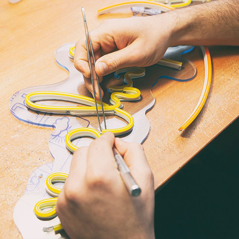 A craftsperson fitting yellow LED neon flex onto a clear acrylic backboard